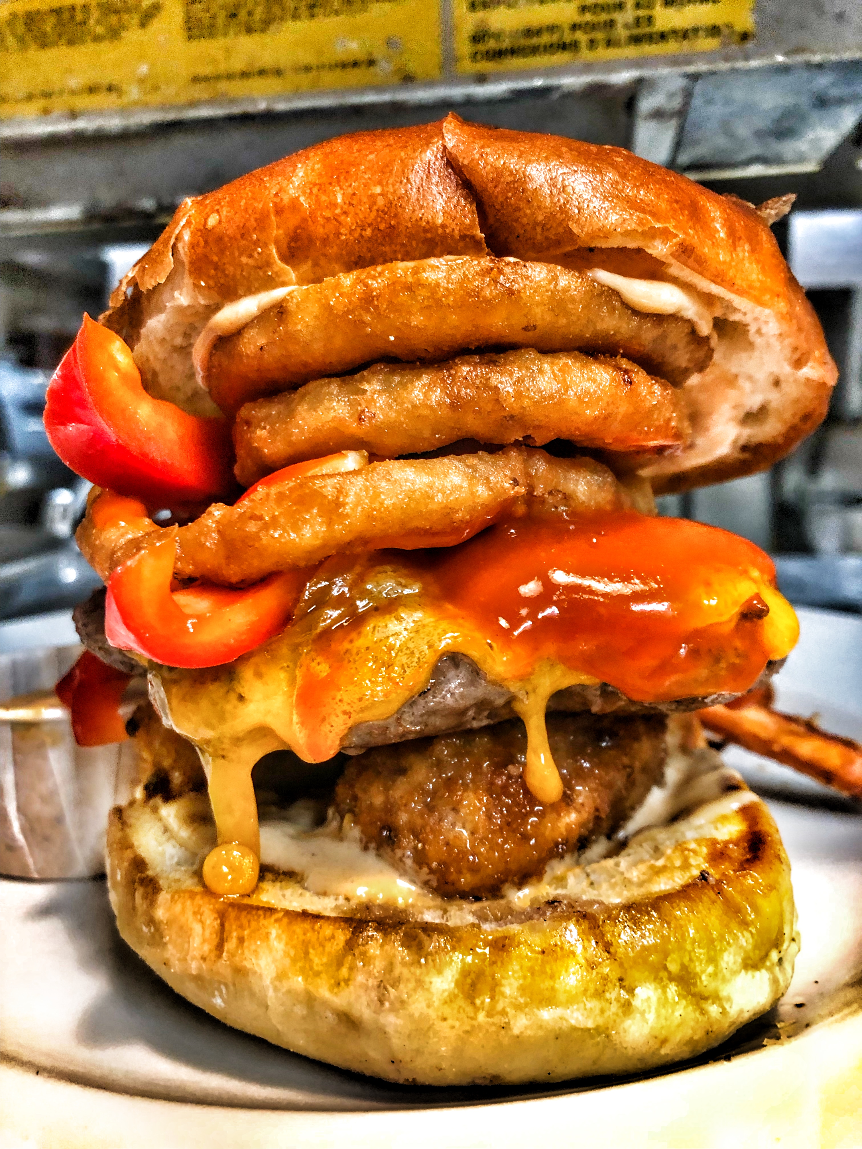 A stacked Wellington Diner burger with onion rings and sauce.